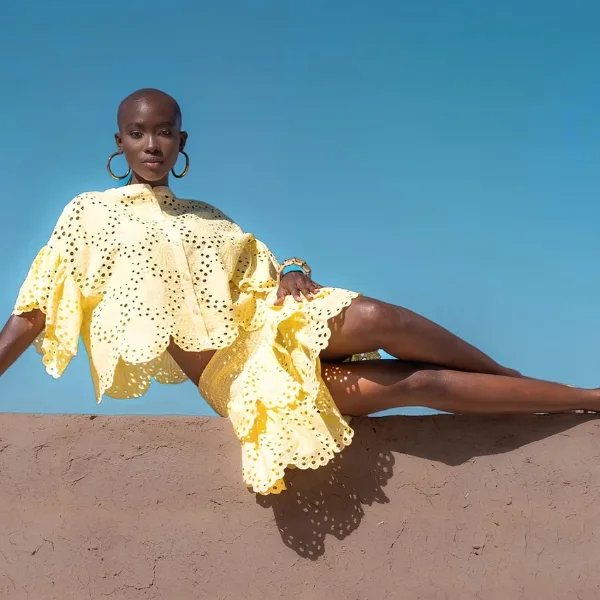 Shooting mode à la Palmeraie Marrakech — robe jaune brodée sur mur en pisé